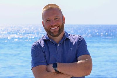 A man with his arms crossed standing on the beach.
