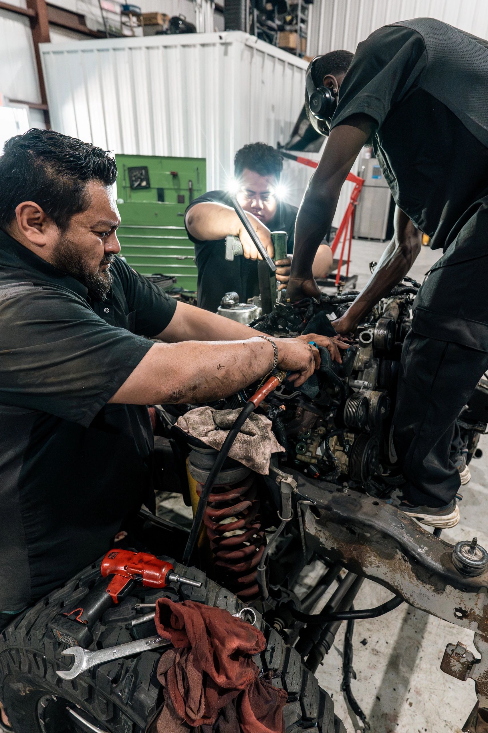 Three mechanics working together on a car engine in a workshop.