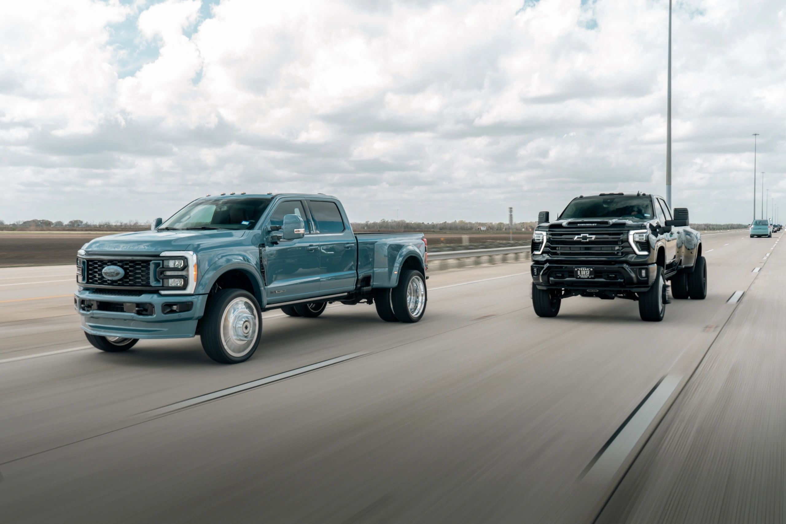 Two large pickup trucks driving side by side on a highway under a cloudy sky.
