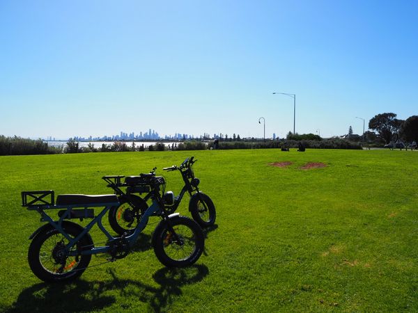 Bikes parked on grass with the sea and Melbourne skyline in the background.