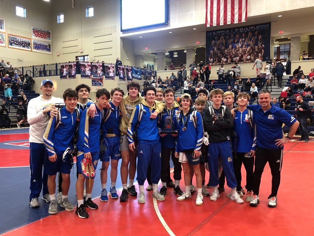 Group of young wrestlers and coaches posing with a trophy.