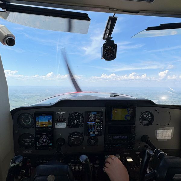 View from inside a small airplane cockpit during flight over a landscape.