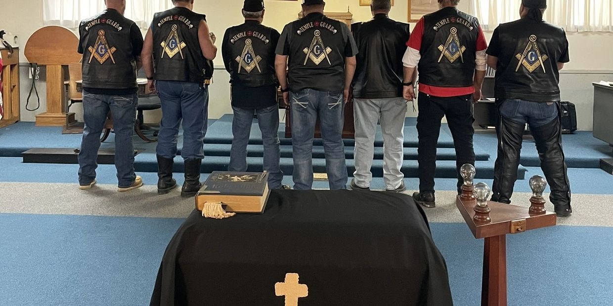 Seven men in matching vests stand in a room with Masonic symbols.