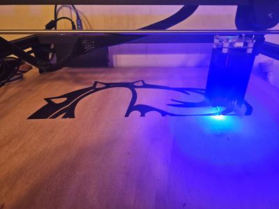 A laser engraver etching a black design onto a wooden surface.