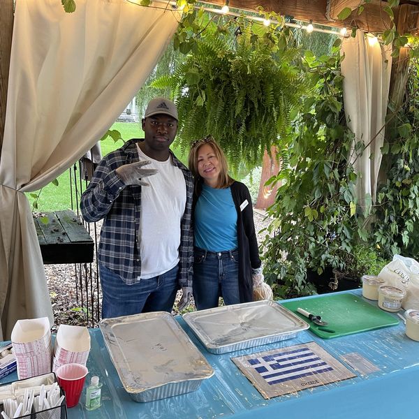 Two people posing at a table under a canopy with greenery.
