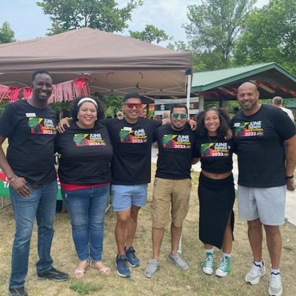 Group of six people smiling outdoors at a Juneteenth Community Celebration in matching shirts.