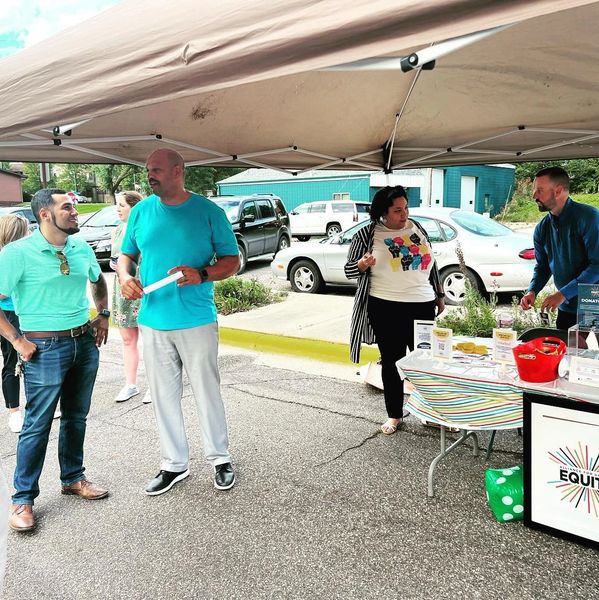People gathered under a canopy at an equity event with a donation table.