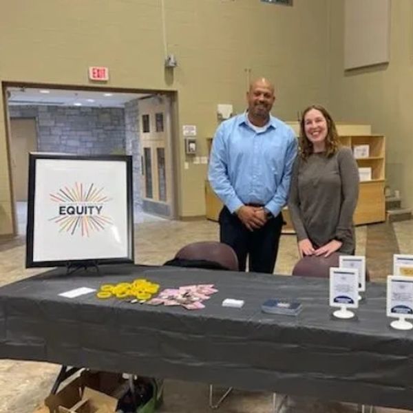 Two people stand behind an equity information table.