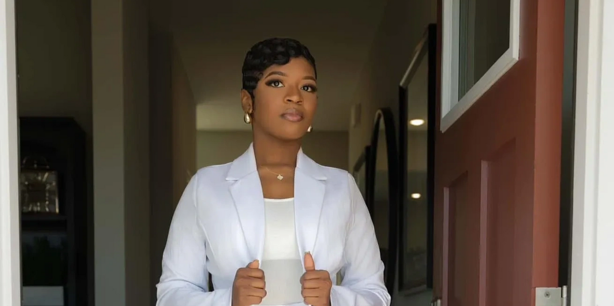 Confident woman in a white suit standing in a doorway.