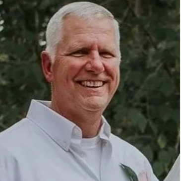 Smiling elderly man in a white shirt outdoors.