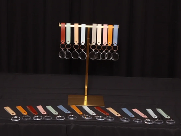 Colorful leather keychains displayed on a brass stand and table against black backdrop.