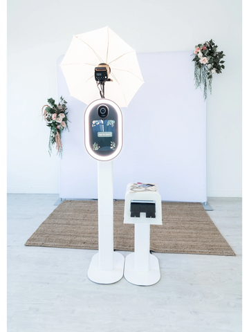 Photo booth setup with camera, light umbrella, and floral decorations.