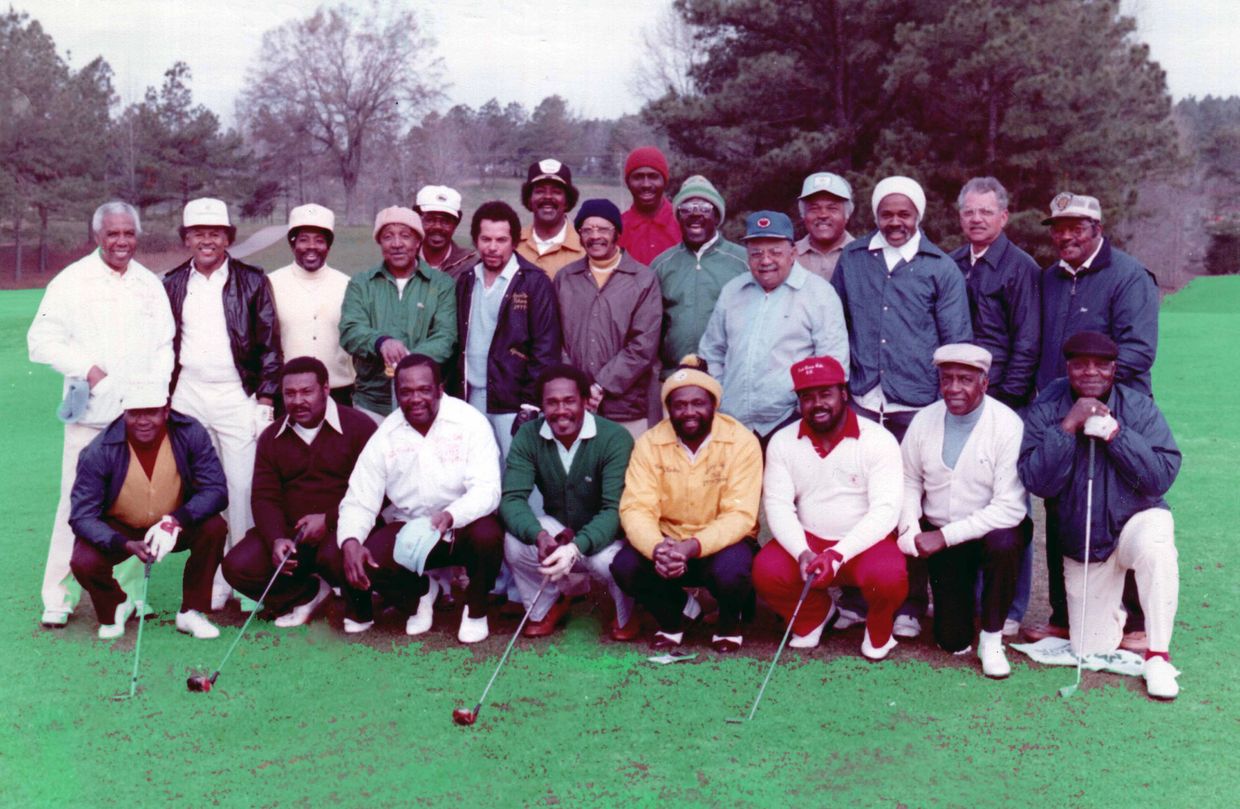 Group of men posing on a golf course, some holding golf clubs.