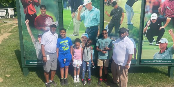 Group of six people posing in front of a golf-themed mural outdoors.