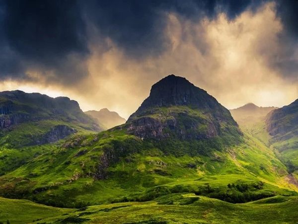 Dramatic clouds hover over lush green mountains at sunset.