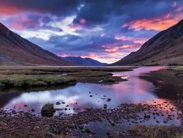 A serene lake reflecting a vibrant, colorful sunset between mountains.
