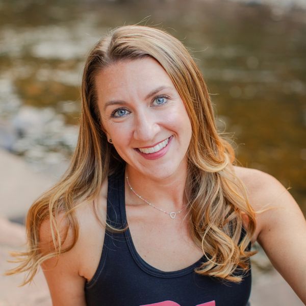 Smiling woman with long blonde hair by a river.