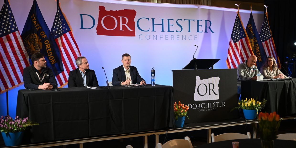Panelists at the Dorchester Conference with Oregon and American flags in the background.