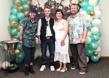 Four people posing together in front of a balloon and floral backdrop.