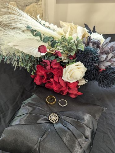 A floral bouquet, two rings, and a black satin pillow with a decorative brooch.