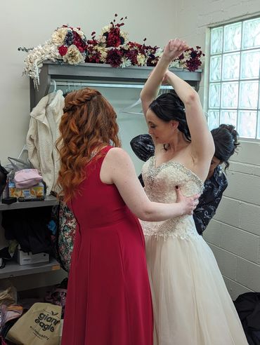 Bride getting help with her wedding dress from bridesmaids in a dressing room.
