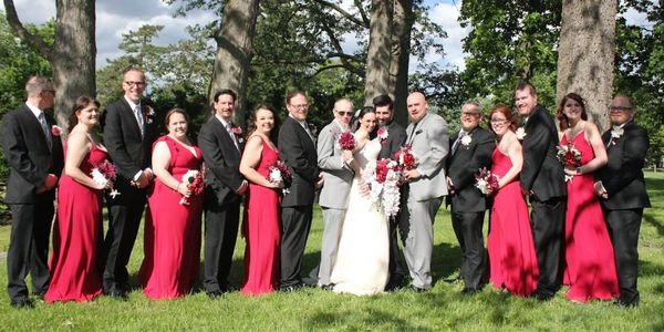 Outdoor photograph of a wedding couple and all the brindesmaids and groomsmen wearing red and black.