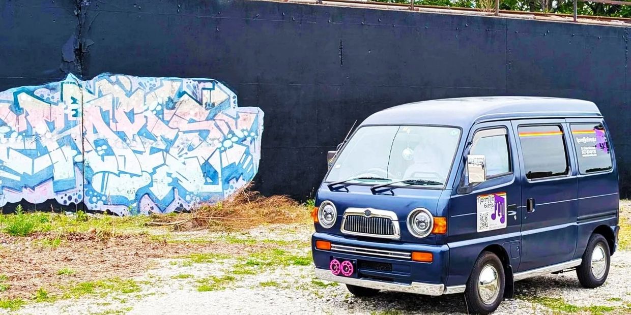 Blue van parked beside a graffiti-covered black wall in an outdoor setting.