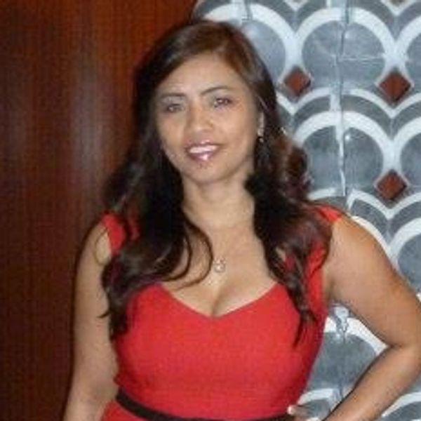 Woman in a red dress posing indoors with a modern sculpture and wooden walls.