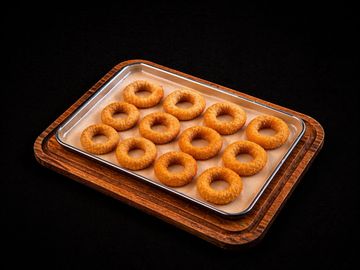 Tray of freshly baked, golden brown ring-shaped cookies on a wooden board.