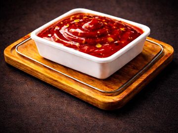 Square white bowl filled with thick red sauce on wooden tray.