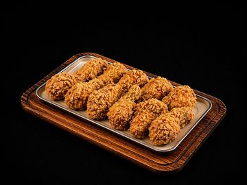 A tray of crispy fried chicken drumsticks on a wooden board.
