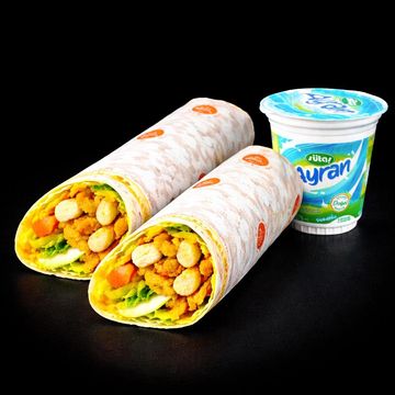 Two chickpea wraps with a cup of ayran on a black background.