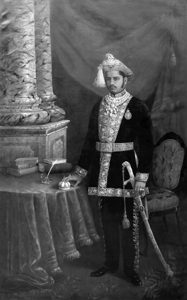 A regal man in traditional royal attire poses formally beside a table with books and a ceremonial sword.
