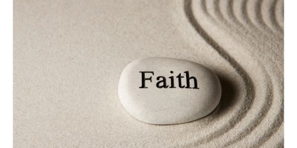 Smooth stone with 'Faith' engraved, resting on raked sand.