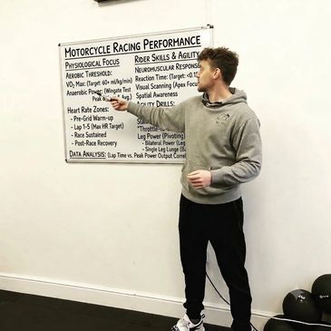 Man pointing at a motorcycle racing performance chart on a wall.