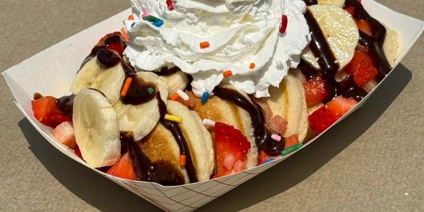 Mini pancakes with banana, strawberries, whipped cream, and chocolate drizzle.