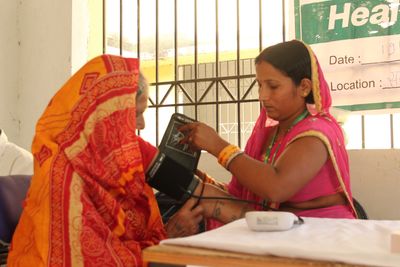 CHE taking blood pressure at a government health camp and supporting doctor–patient communication.
