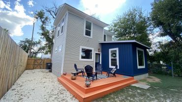 Two-story house with a wooden deck and outdoor chairs.