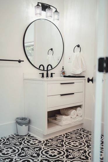 Modern bathroom vanity with round mirror and patterned floor tiles.