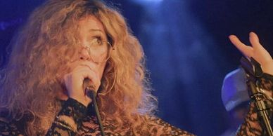 Woman with curly hair singing passionately into a microphone.