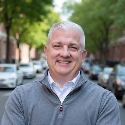 Smiling middle-aged man with gray hair outdoors on a street.