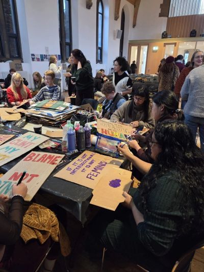 People gathered indoors making colorful protest signs on cardboard.