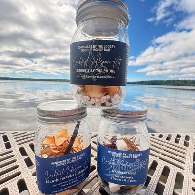 Three cocktail mix jars stacked on a dock by a lake under a blue sky.