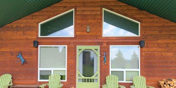 Cozy wooden cabin porch with green Adirondack chairs and decorative wall art.