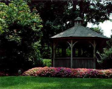 Wooden gazebo surrounded by pink flowers.