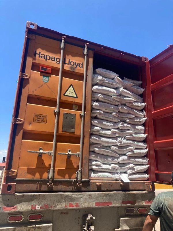 Open shipping container loaded with stacked white sacks under clear blue sky.