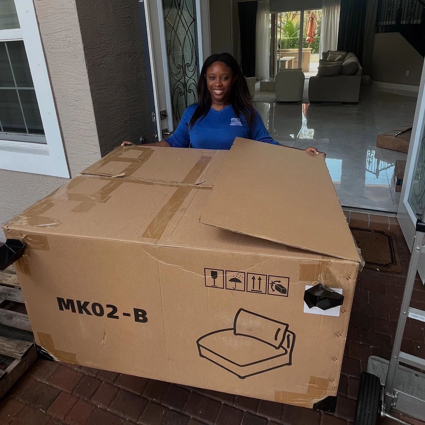 A woman smiling behind a large cardboard box labeled MK02-B.