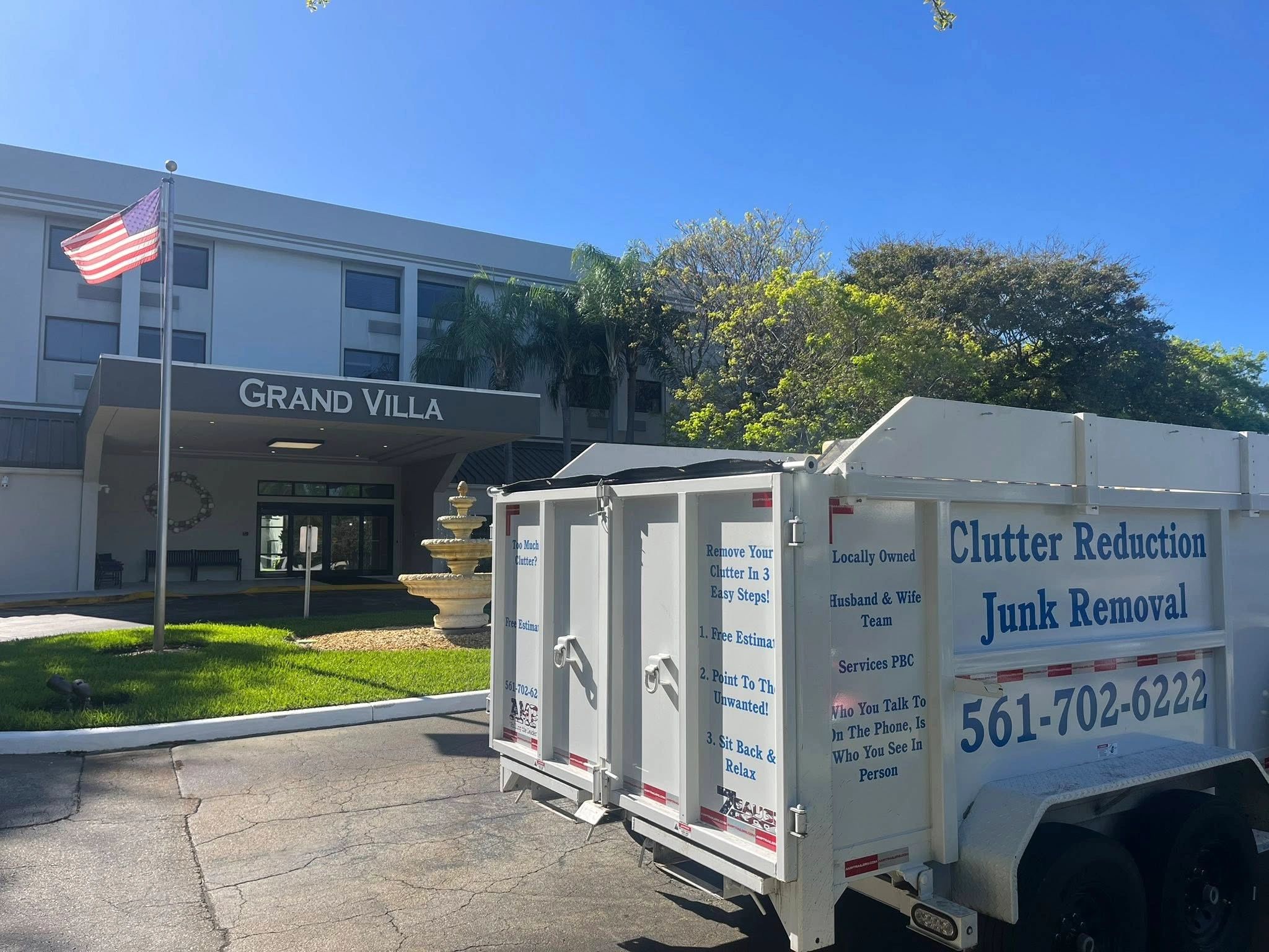 Junk removal truck outside Grand Villa building on a sunny day.