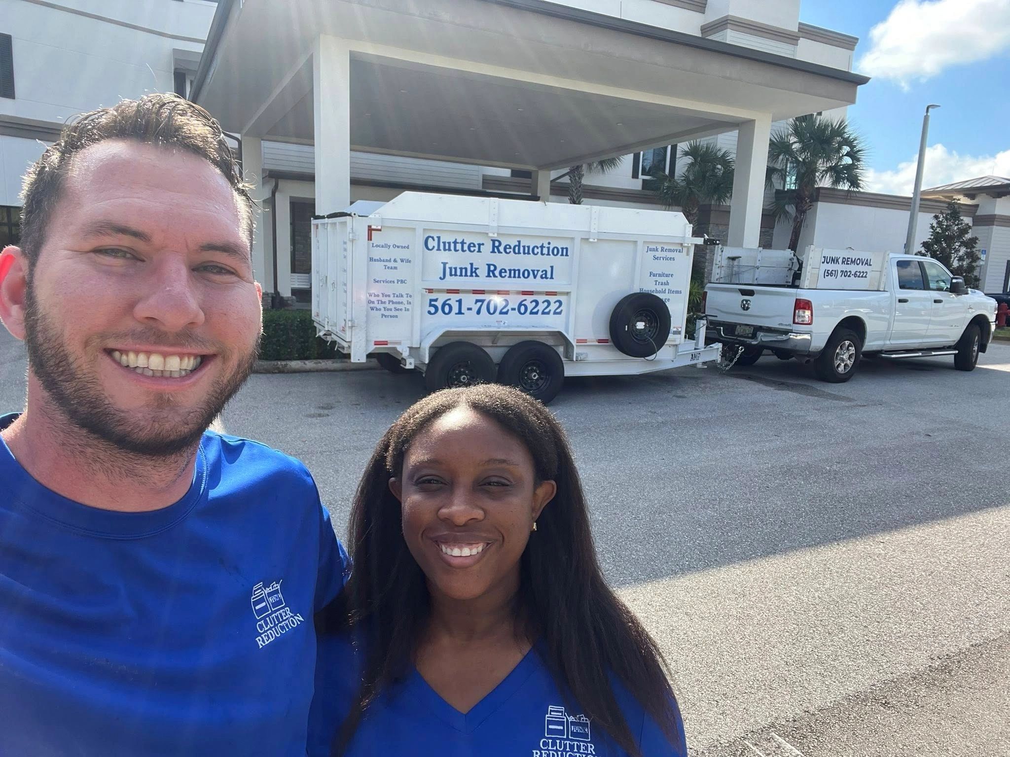 Two people smiling in front of a clutter removal truck and trailer.