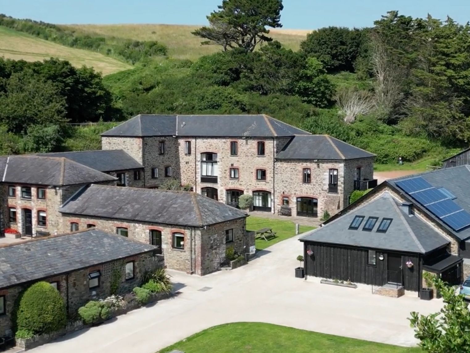 Stone buildings with solar panels in a lush green countryside setting.